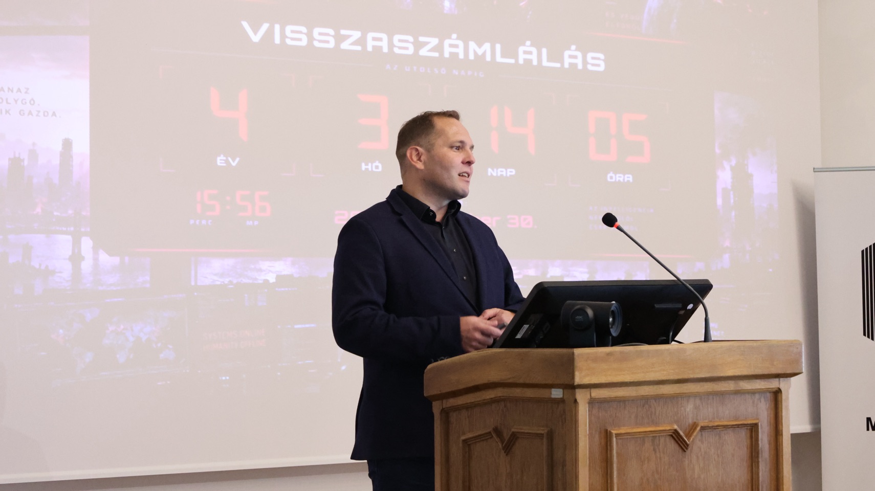 Előadó a konferencia pulpitusánál, visszaszámlálást bemutató vetítéssel.