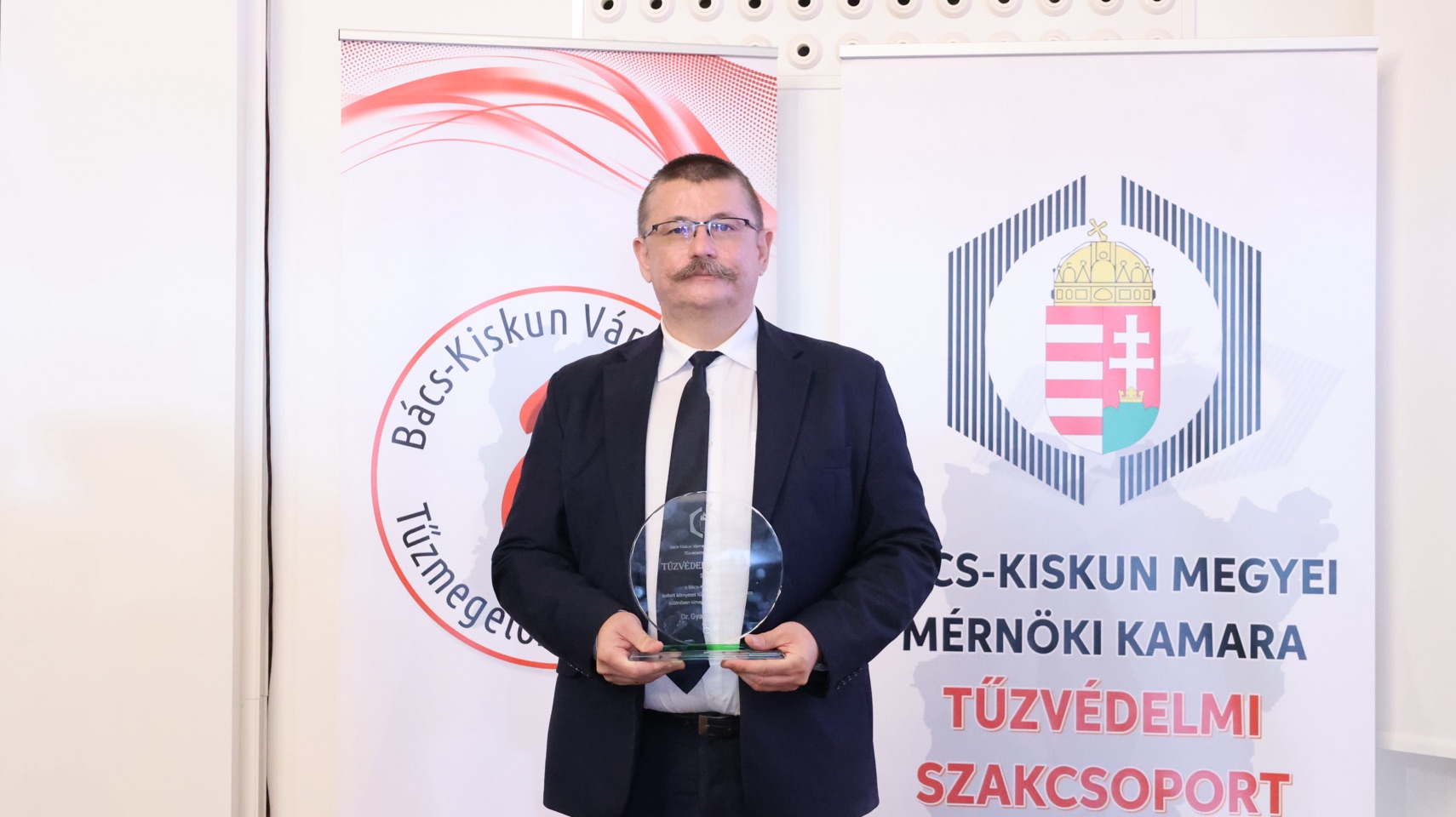 Portré a Tűzvédelmi Nívódíj üvegplakettjével a kamarai molinók előtt.